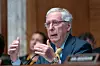 Mitch McConnell sitter ved et bord i en høringssal og snakker mens han gestikulerer.