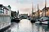 Båter langs en kanal med bygninger på begge sider under en lys himmel.