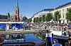Havna i Arendal med båter, en kirke i bakgrunnen og mange mennesker langs kaia.