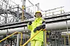 Person i gul vernedress står foran rør og industrielt anlegg på Mongstad.