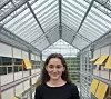 Sara Fakhraee (Stipendiat) står foran et lyst glassbygg med høyt glasstak og gule markiser.