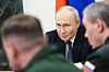 Vladimir Putin sitter ved et møtebord, med to utviskede personer i forgrunnen.