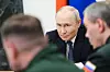 Vladimir Putin sitter ved et møtebord, med to utviskede personer i forgrunnen.