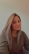 En kvinne med langt lyst hår sitter foran en lys vegg og ser mot kamera.