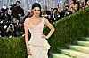 Kylie Jenner i lys, drapert kjole på Met-gallaen foran fotografer og en grønn hekk.