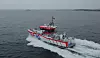 Rød og hvit redningsbåt med RIB-merking går i høy fart over åpent hav.