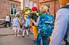 Skolebarn med fargerike sekker samles i skolegården ved en rød teglsteinsbygning.