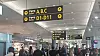 Flyplasshall med mange passasjerer og gule avgangsskilt hengende fra taket.