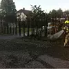 Brannmann med slange sprøyter vann mot røyk i et område nær trær og en bolig.