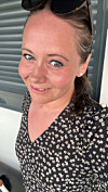 Nærbilde av en kvinne som smiler svakt foran en grå vegg.