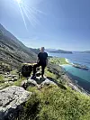 En person står på en stein i fjellsiden med hav, øyer og blå himmel i bakgrunnen.