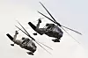 To Black Hawk-helikoptre fra Alaska Army National Guard flyr tett i formasjon mot lys himmel.