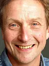 Nærbilde av en smilende mann med blå skjorte mot nøytral bakgrunn.