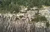 Bratt fjellvegg med en liten hylle og redningsarbeidere som er synlige høyt oppe i terrenget.