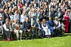 Kongefamilien sitter på rekke under en hagefest i Slottsparken omgitt av mange gjester.