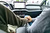 To menn holder hender i baksetet på en bil med skjerm og dashbord i forgrunnen.