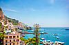Panoramautsikt over Amalfi med pastellfargede bygninger, havn, båter og blått hav langs Amalfikysten.