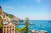 Panoramautsikt over Amalfi med pastellfargede bygninger, havn, båter og blått hav langs Amalfikysten.
