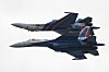 To Sukhoi Su-35S-jagerfly flyr tett sammen mot lys himmel under en flyoppvisning.