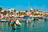 Fargerike luzzu-båter ligger i havnen ved Marsaxlokk på Malta, med kirketårn og sjø i bakgrunnen.