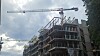 Byggeplass med stillas, halvferdig bygg og to tårnkraner mot overskyet himmel.