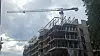 Byggeplass med stillas, halvferdig bygg og to tårnkraner mot overskyet himmel.