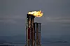Flammer brenner fra et tårn ved Kårstø prosessanlegg med fjord og fjell i bakgrunnen.