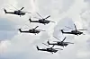 Fem russiske militærhelikoptre flyr i formasjon mot en lys himmel.