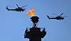 To russiske militærhelikoptre flyr over en rostral-kolonne med flamme mot blå himmel.