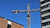 Byggekran mellom en murbygning og et moderne høyhus under blå himmel.