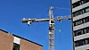 Byggekran mellom en murbygning og et moderne høyhus under blå himmel.