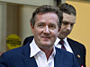 Piers Morgan i dress foran en bygning, med en mann like bak seg.