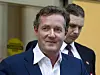 Piers Morgan i dress foran en bygning, med en mann like bak seg.