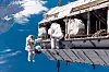To astronauter arbeider utenfor romstasjonen, med jorden og Stillehavet synlig i bakgrunnen.