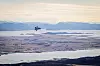 Et F-35A-fly flyr over et flatt vinterlandskap med fjord og fjell i bakgrunnen.