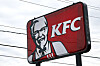 Rødt KFC-skilt med oberst Sanders-portrett mot en overskyet himmel og kraftledninger.