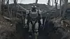 Humanoid robot står i en grøft omgitt av bare trær og skogbunn.