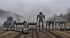 Flere robotlignende maskiner står på rekke på en gjørmete vei i tåke.