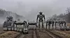Flere robotlignende maskiner står på rekke på en gjørmete vei i tåke.