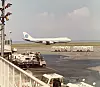 Passasjerfly på bakken med servicekjøretøy og flyplassterminal i bakgrunnen.