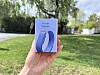 En hånd holder esken til Google Fitbit Air med bilde av et lavendelfarget treningsarmbånd i en hage.