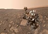 Mars-rover med robotarm på steinete, støvete slette under lys himmel.