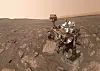 Mars-rover med robotarm på steinete, støvete slette under lys himmel.