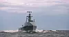 Grått marinefartøy seiler gjennom bølger under overskyet himmel.
