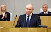 Vladimir Putin taler fra talerstol i Statsdumaen i Moskva, med to personer i bakgrunnen.