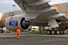 Person i oransje arbeidsklær går ved motoren på et stort passasjerfly på bakken.