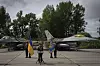Volodymyr Zelenskyj taler foran to F-16-fly, flankert av soldater med ukrainske flagg.