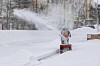 Person i mønstret vinterklær ved rail mens snø spruter over et snødekt område.
