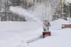 Person i mønstret vinterklær ved rail mens snø spruter over et snødekt område.