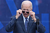 Joe Biden tar av seg solbrillene foran en blå bakgrunn under en seremoni i Chicago.